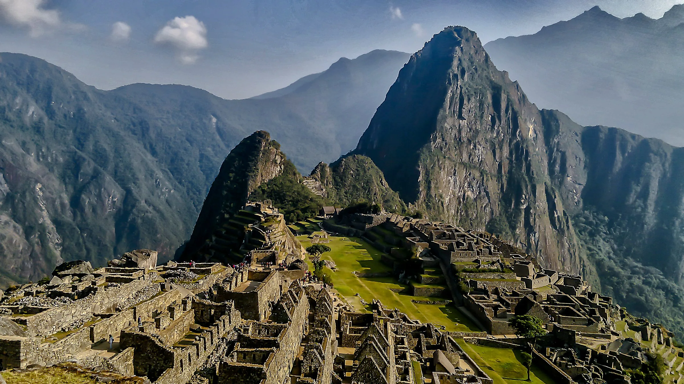 Machu Picchu terraces and stone structures seen across the green Andean ridge.